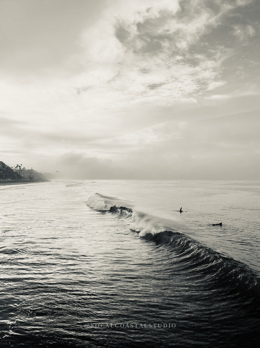 Black and white ocean photo of two surfers watching a wave break.